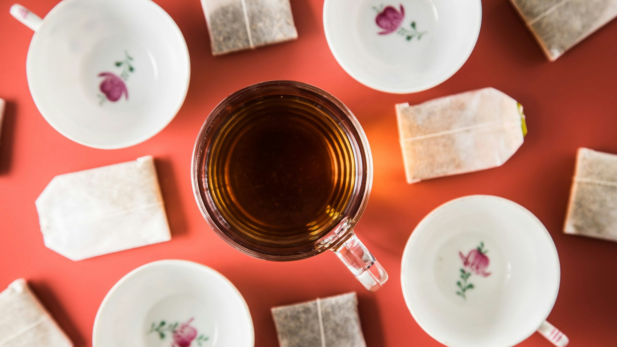 Um eine volle Tasse Tee herum stehen weitere leere Teetassen und liegen Teebeutel