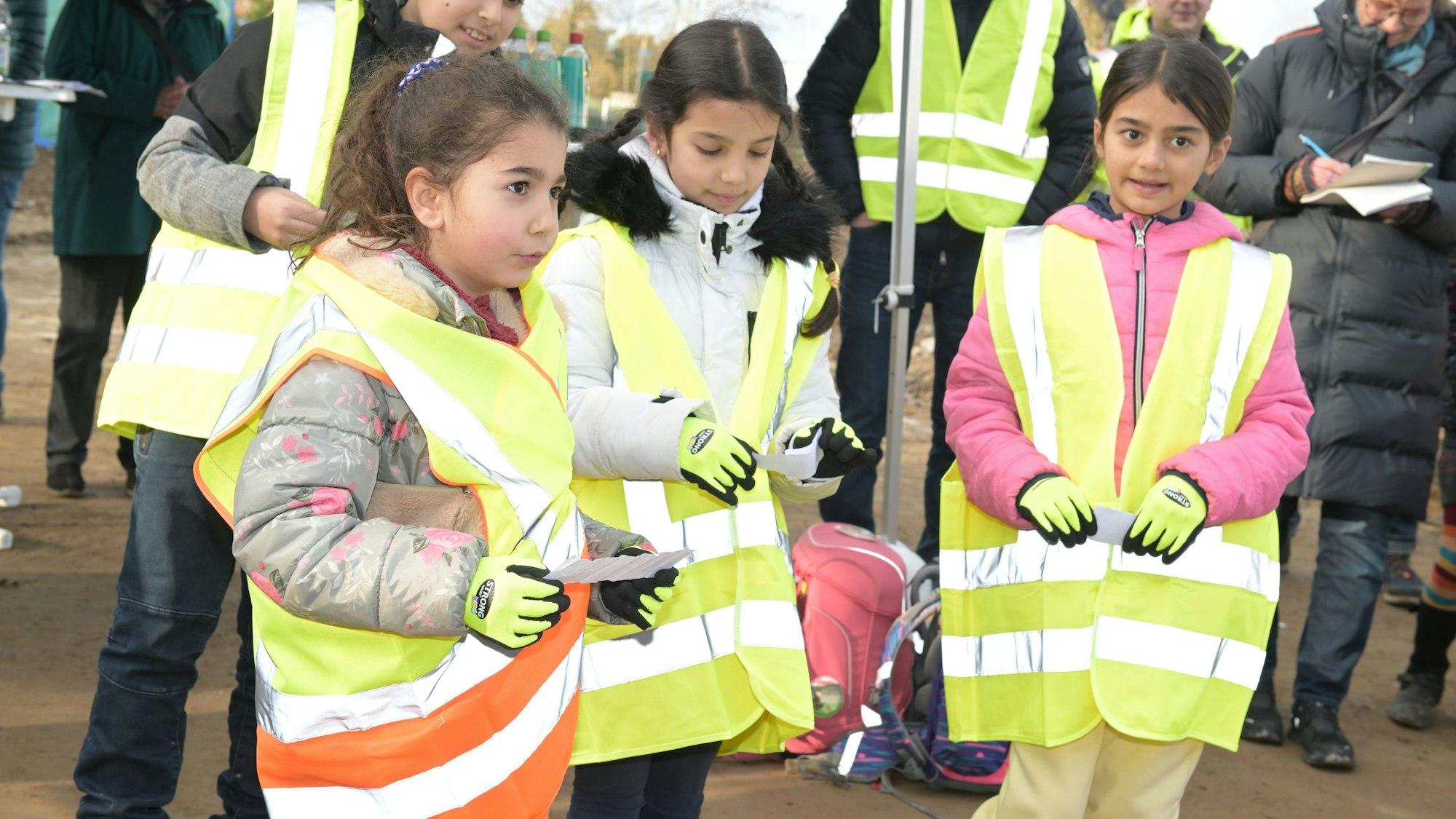 Drei junge Mädchen stehen in gelben Warnwesten auf der Baustelle.