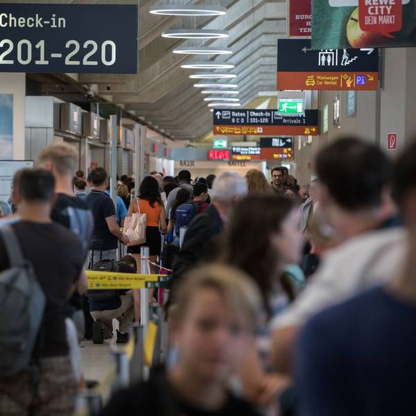 Zahlreiche Passagiere warten am Flughafen Köln/Bonn an der Sicherheitskontrolle. Es ist ein Schild mit Hinweisen zum Check-in zu sehen.