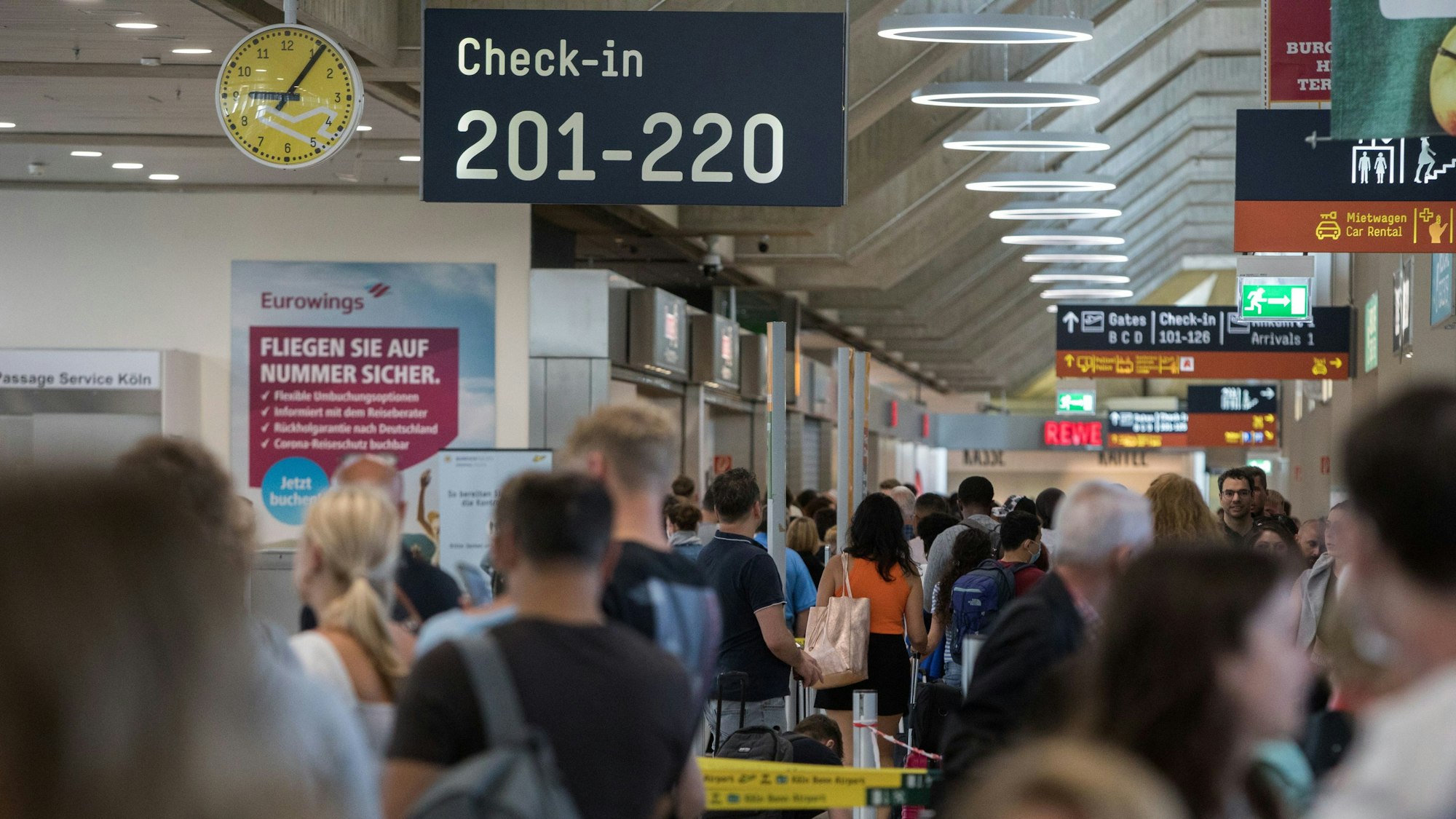 Zahlreiche Passagiere warten am Flughafen Köln/Bonn an der Sicherheitskontrolle. Es ist ein Schild mit Hinweisen zum Check-in zu sehen.
