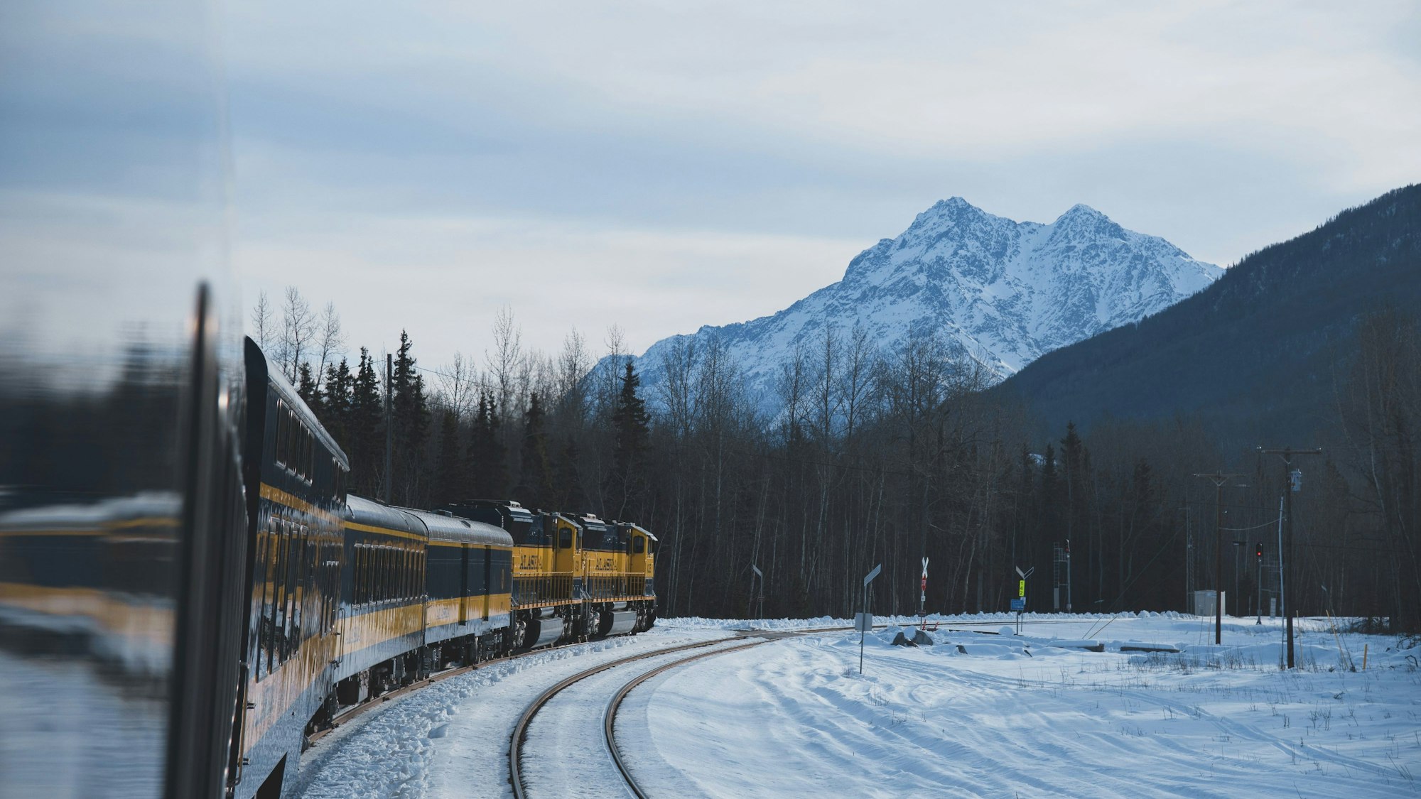 Auf den verschneiten Schienen der Alaska Railroad fährt ein Zug, im Hintergrund ein verschneiter Berggipfel