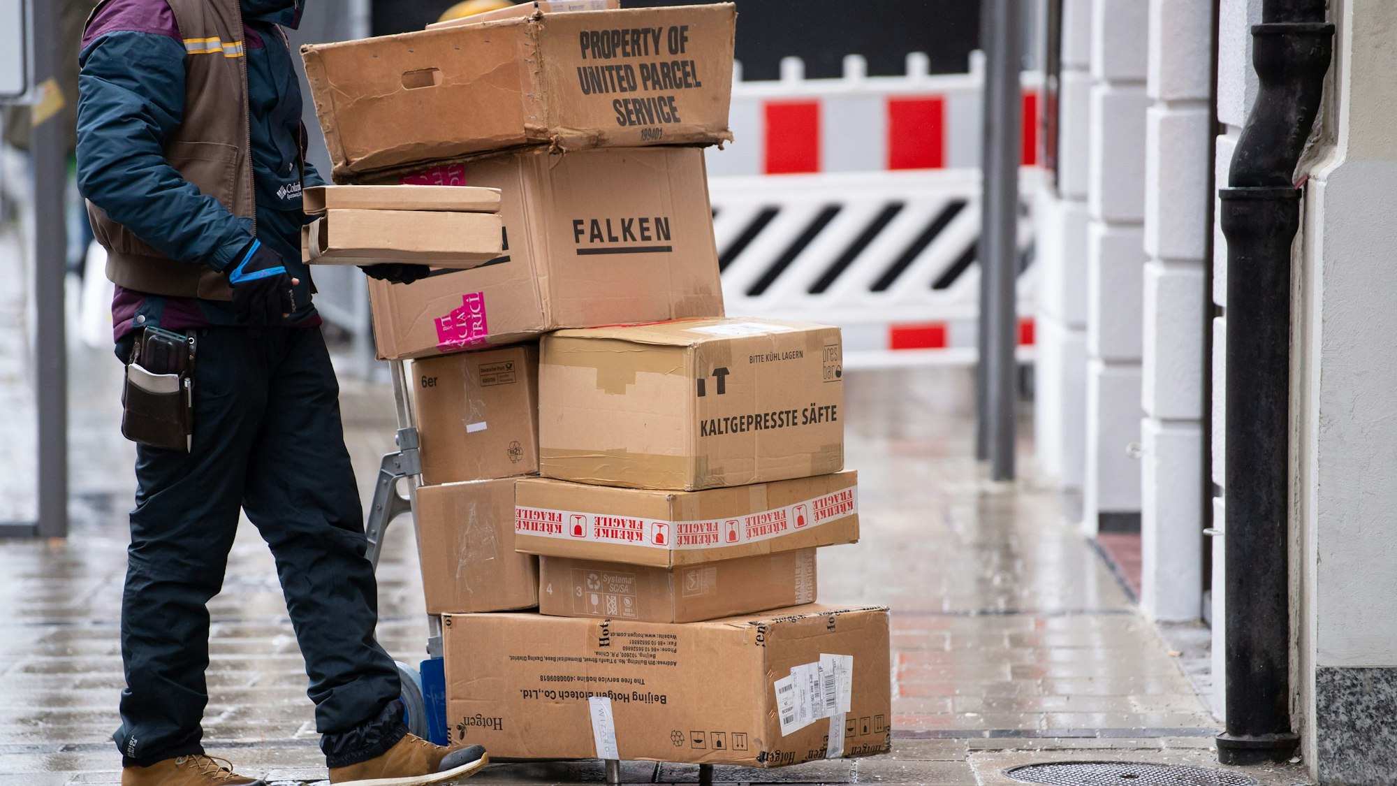 Ein Paketbote liefert Pakete aus. Er hat einige Pakete auf einer Sackkarre gestapelt.