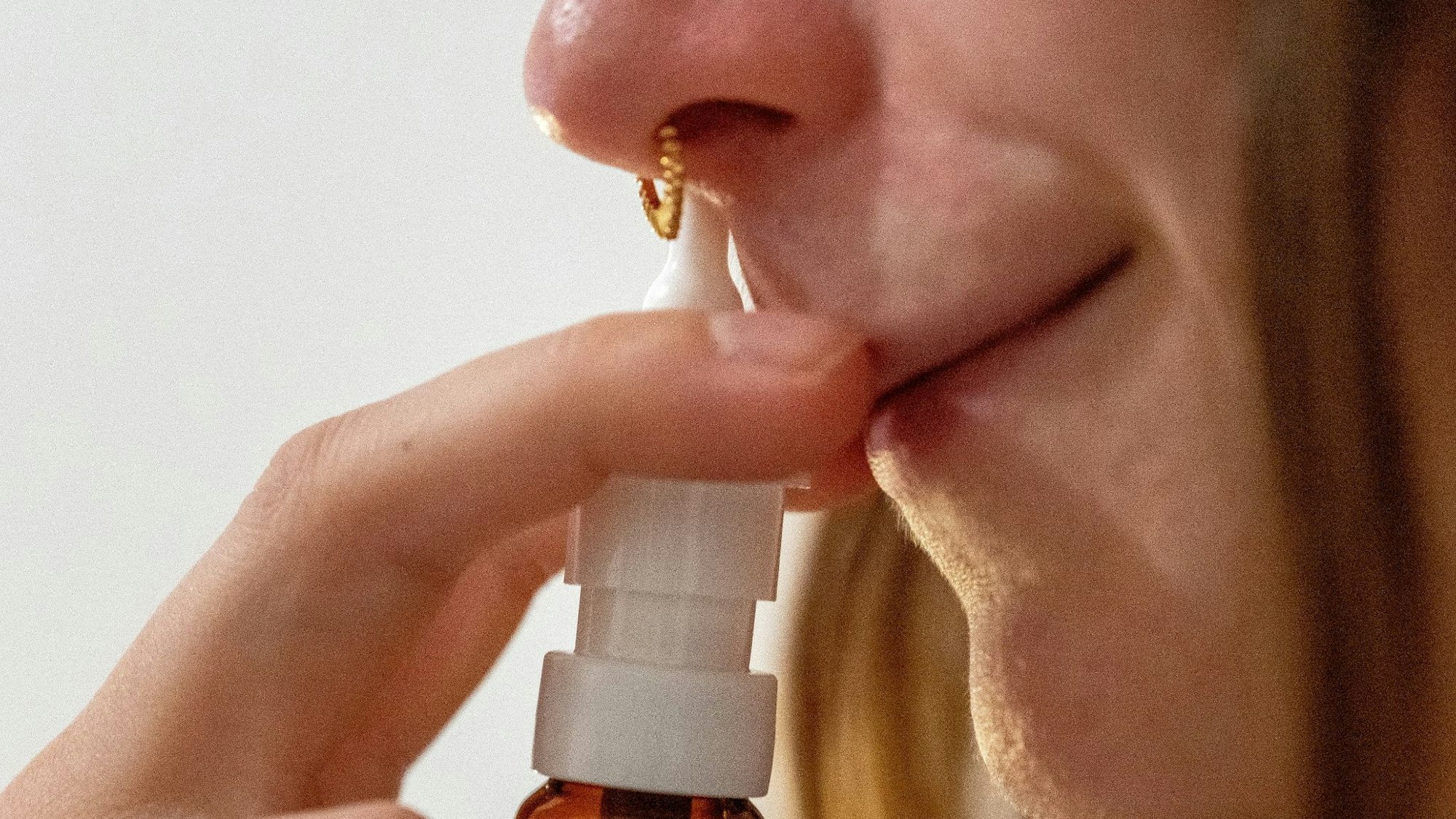 Eine Frau hält sich eine Flasche Nasenspray an das rechte Nasenloch.