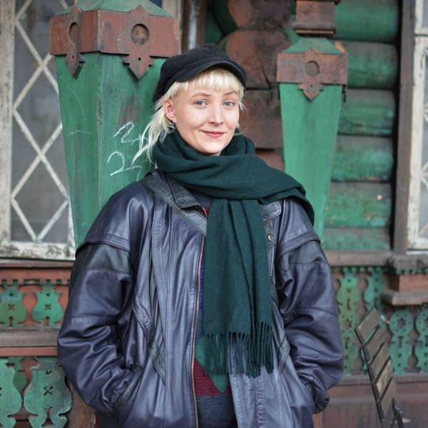 Nine Mai steht vor einer Kulisse eines alten verwitterten Hauses. Sie hat kurze blonde Haare und eine Kappe auf.