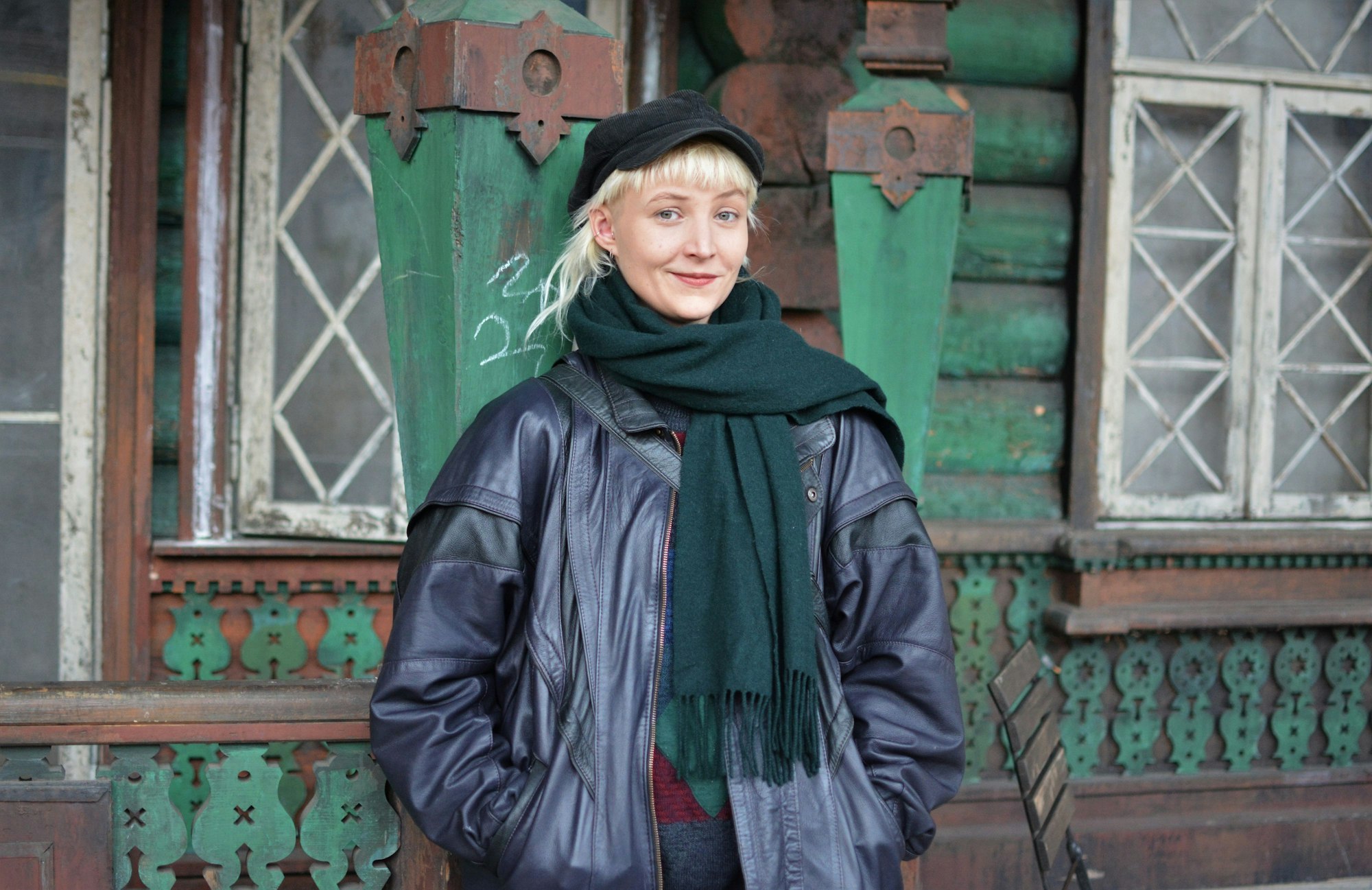 Nine Mai steht vor einer Kulisse eines alten verwitterten Hauses. Sie hat kurze blonde Haare und eine Kappe auf.