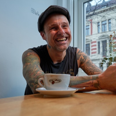 Ingo Knollmann lachend am Tisch im Café. Vor ihm steht eine Tasse Kaffee.