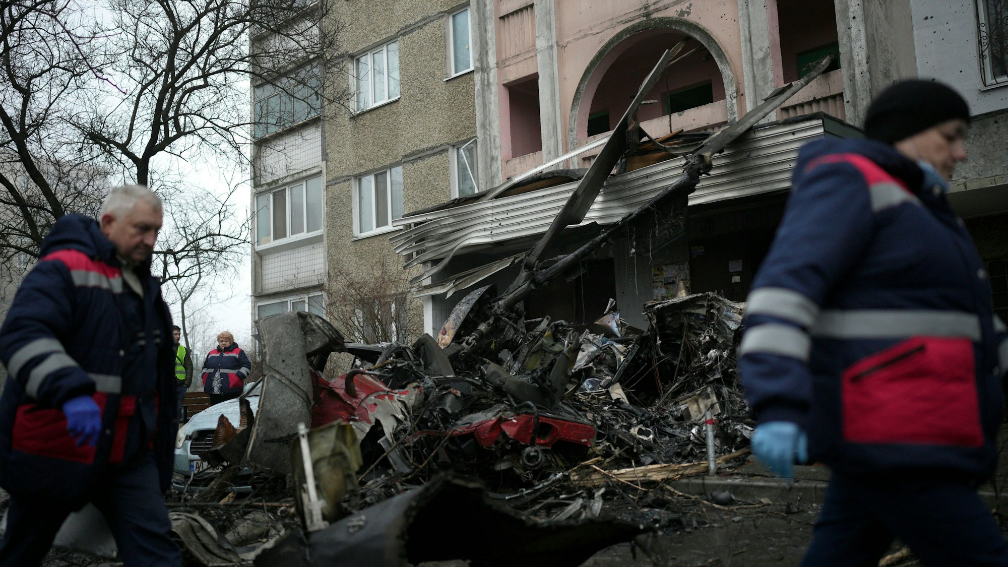 Arbeiter gehen an der Absturzstelle eines Hubschraubers auf zivile Infrastruktur in Brovary vorbei.