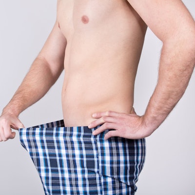 Ein Mann zieht die Unterhose nach vorne und blickt auf sein Geschlechtsteil.