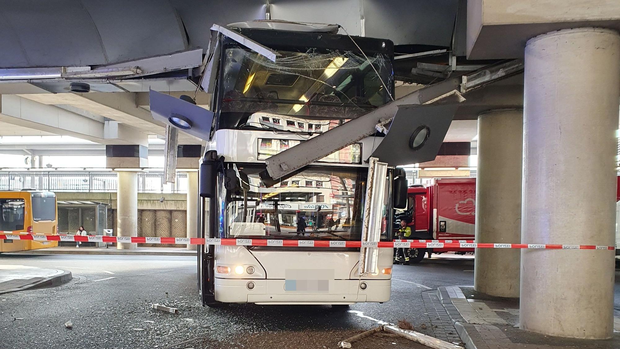 Ein Doppeldeckerbus hat eine zerstörte Scheibe, Teile der Decke hängen runter, der Bereich ist mit einem Polizeiband abgesperrt.