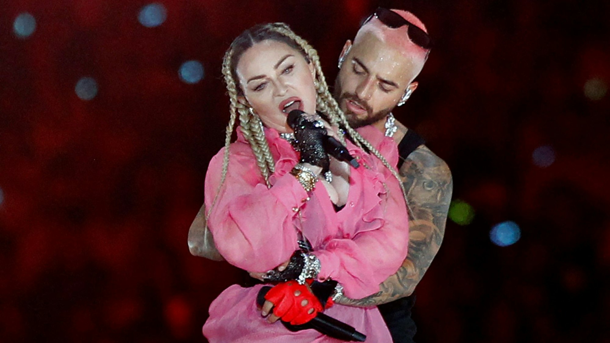 Madonna bei einem Live-Auftritt mit Sänger Maluma hinter ihr. Sie singt in ein Mikro.