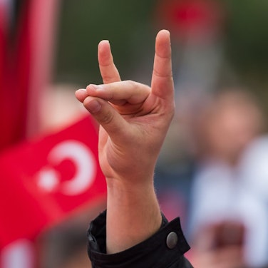 Eine Hand zeigt den "Wolfsgruß" der Grauen Wölfe während einer Pro-Türkischen Demonstration. Im Hintergrund wehen Türkeiflaggen.