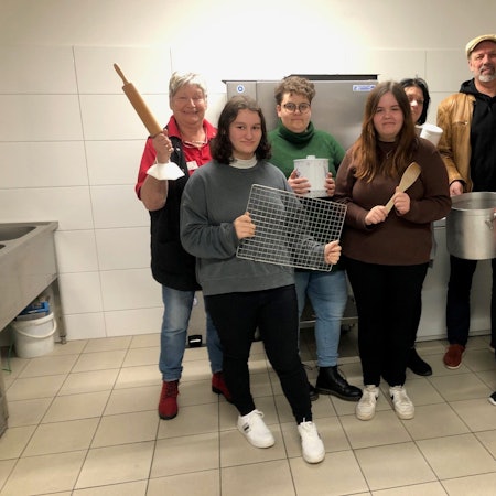 Die Teilnehmerinnen und Teilnehmer des „Bunt und gesund“-Projekts stehen in der Küche der Jugendeinrichtung und halten Koch-Utensilien in ihren Händen.