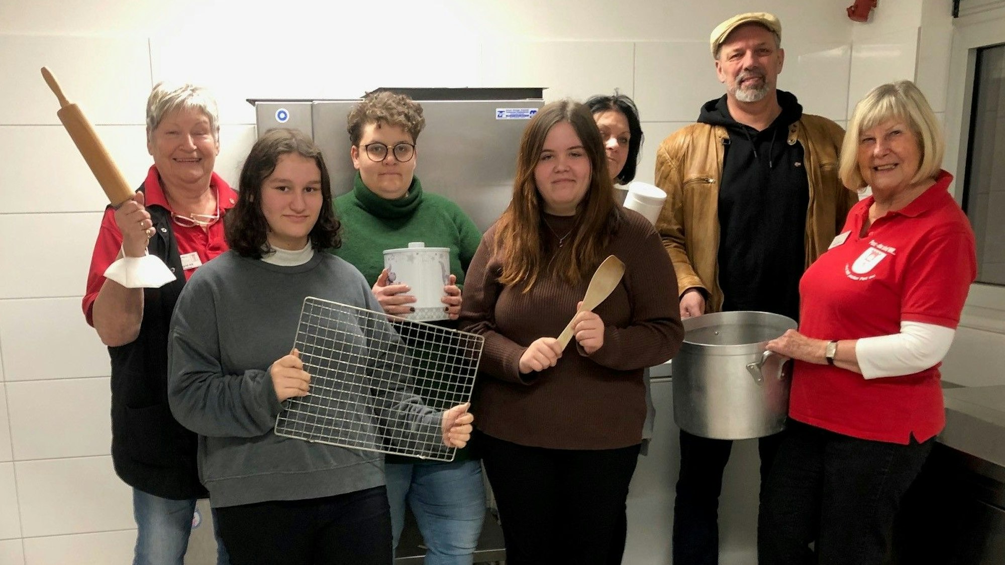 Die Teilnehmerinnen und Teilnehmer des „Bunt und gesund“-Projekts stehen in der Küche der Jugendeinrichtung und halten Koch-Utensilien in ihren Händen.