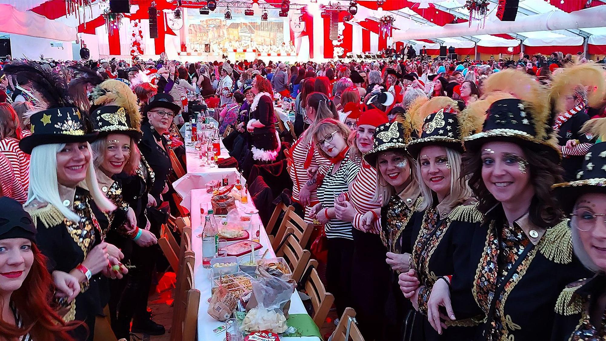 Kostümierte Damen stehen im Festzelt an einem Tisch und haben sich zum Schunkeln untergehakt.