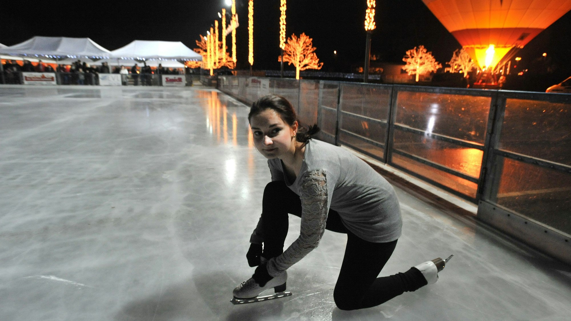Ein Mädchen schnürt ihre Schlittschuhe auf der Eislaufbahn