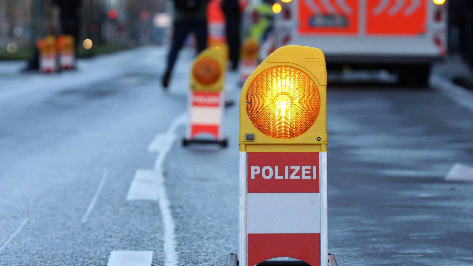 Eine Warnbarke mit der Aufschrift „Polizei“ steht vor einem Rettungswagen an einer abgesperrten Unfallstelle. (Symbolbild)