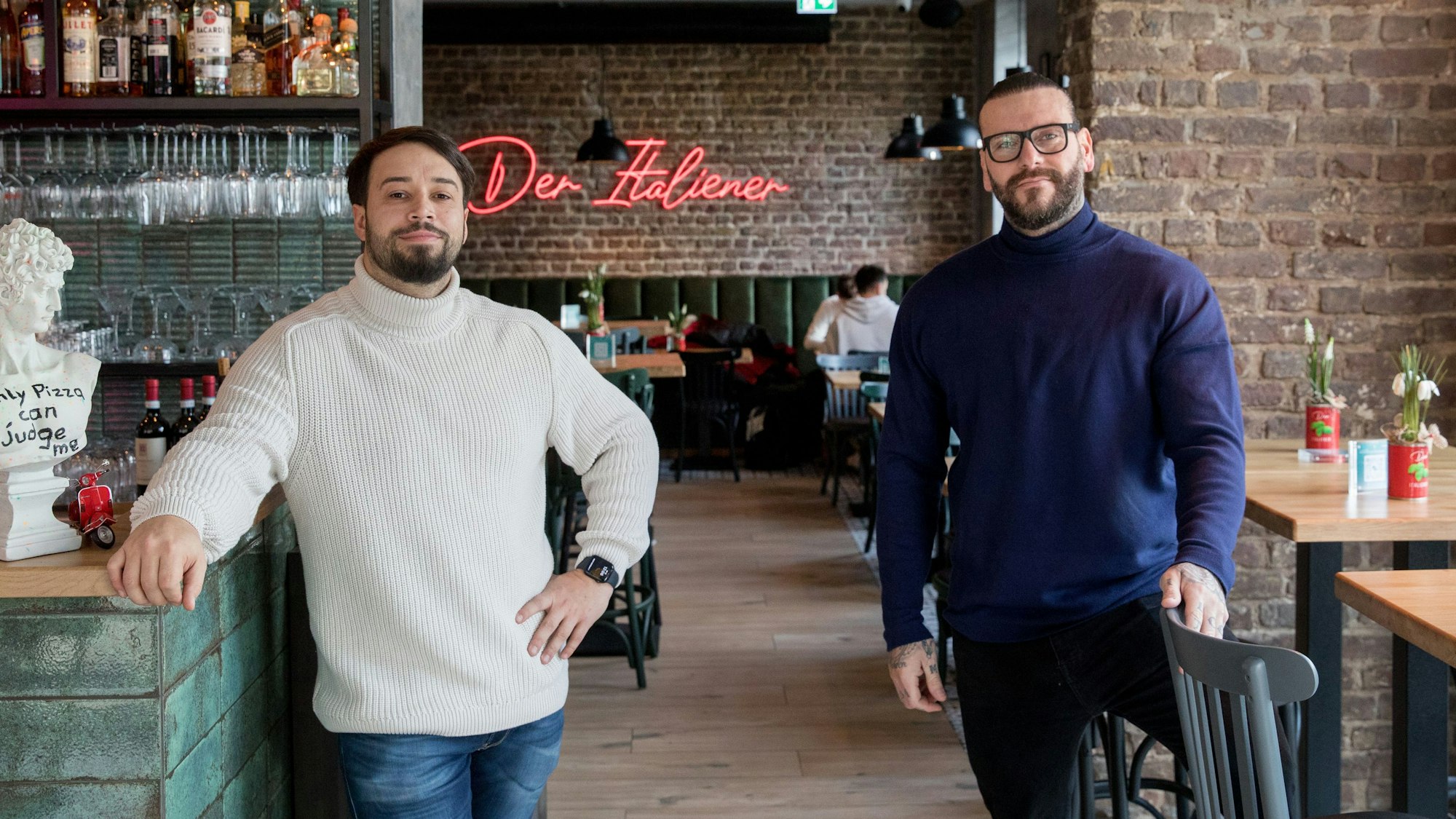 Nermin Music (links) und Marco Baron stehen in ihrem Restaurant, im Hintergrund sieht man an der Backsteinwand einen Neon-LED-Schriftzug mit "Der Italiener".
