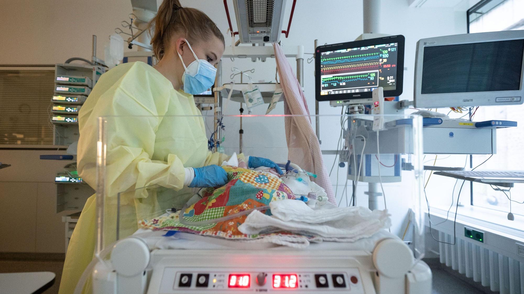 Das Bild zeigt eine Intensivpflegerin, die auf einer Kinder-Intensivstation einen kleinen Patienten versorgt, der beatmet wird.