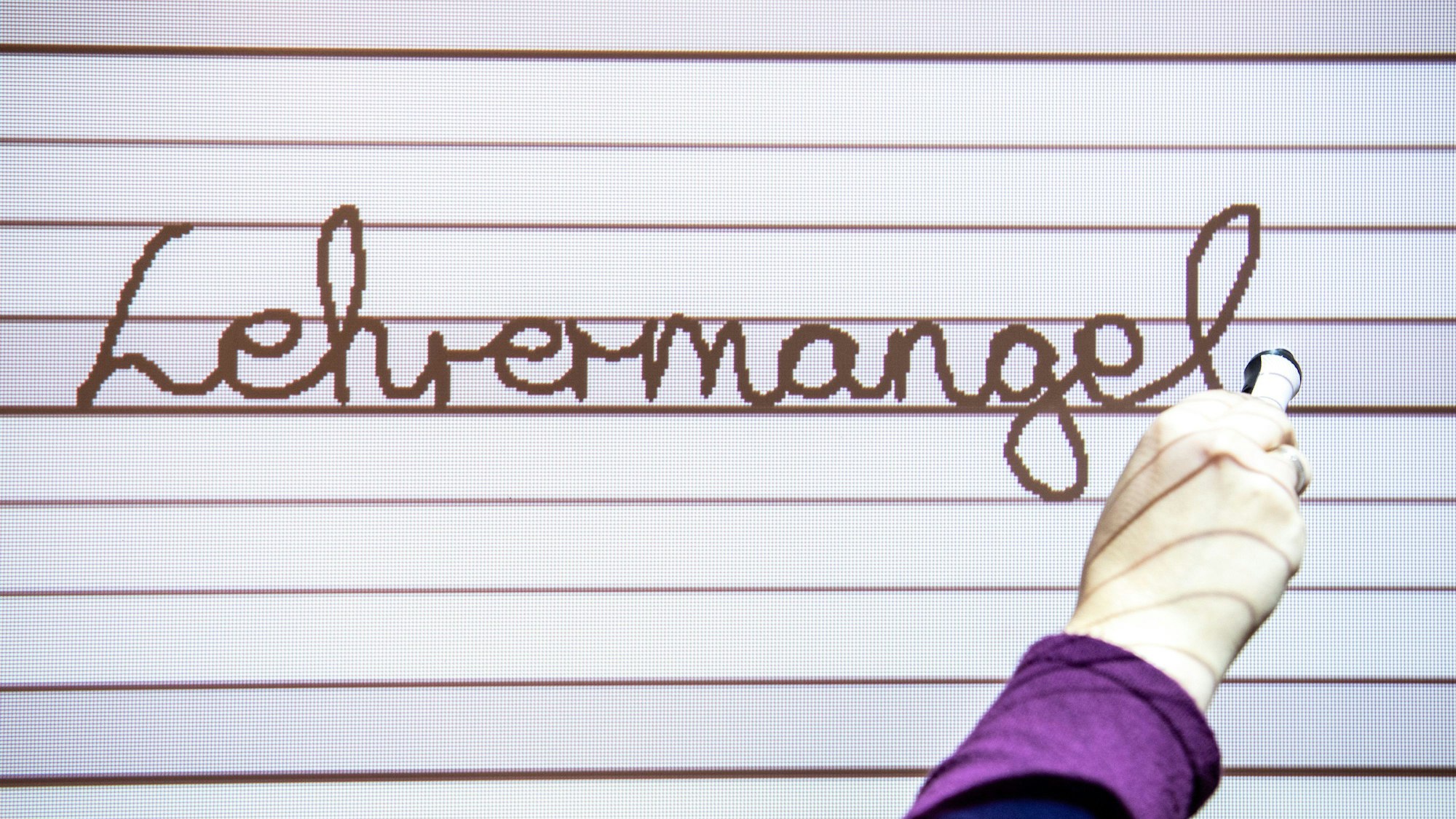 Eine Lehrerin schreibt auf ein Whiteboard in einer Grundschule das Wort Lehrermangel.