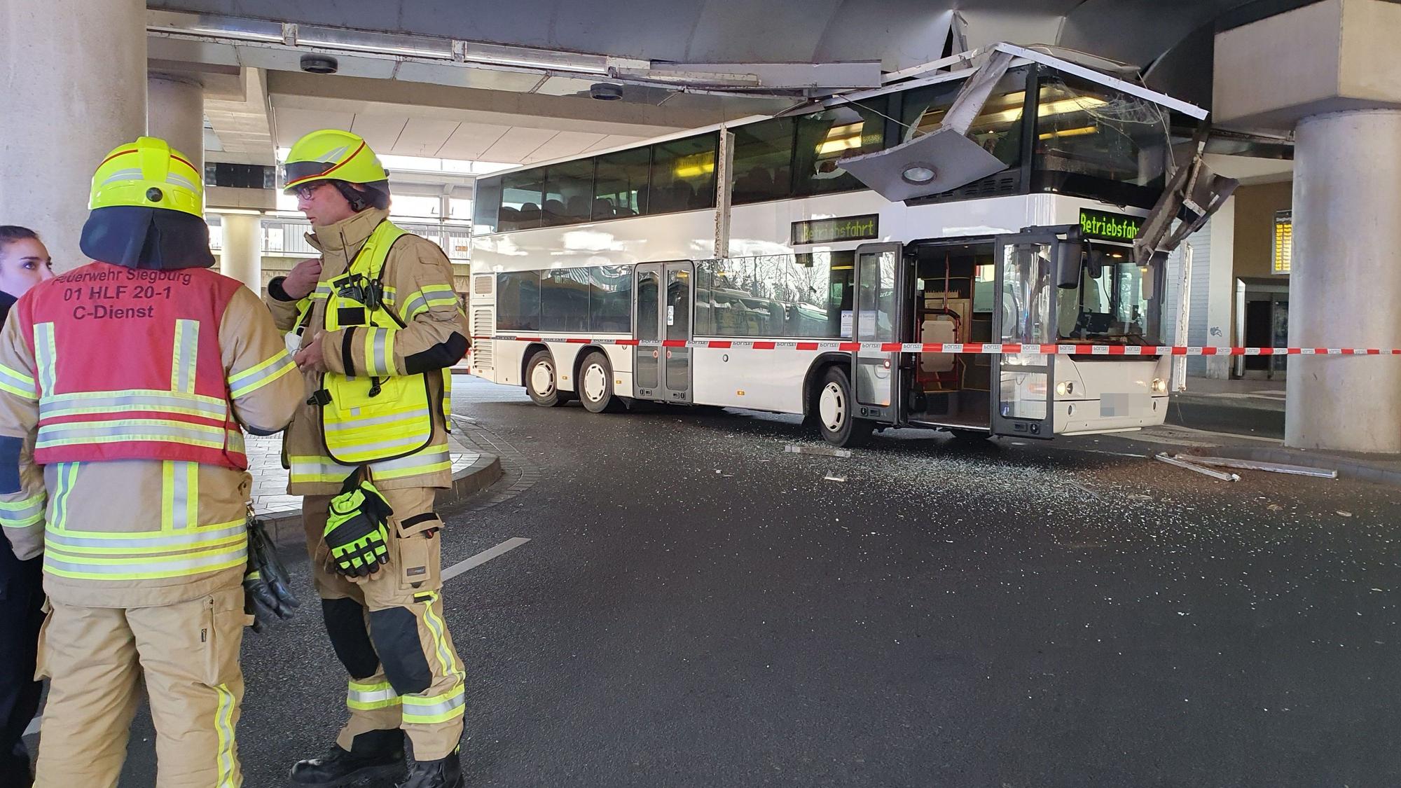 Feuerwehrleute stehen an der Seite, dahinter steht ein Doppeldeckerbus, der sich in einer Unteführung festgefahren hat.
