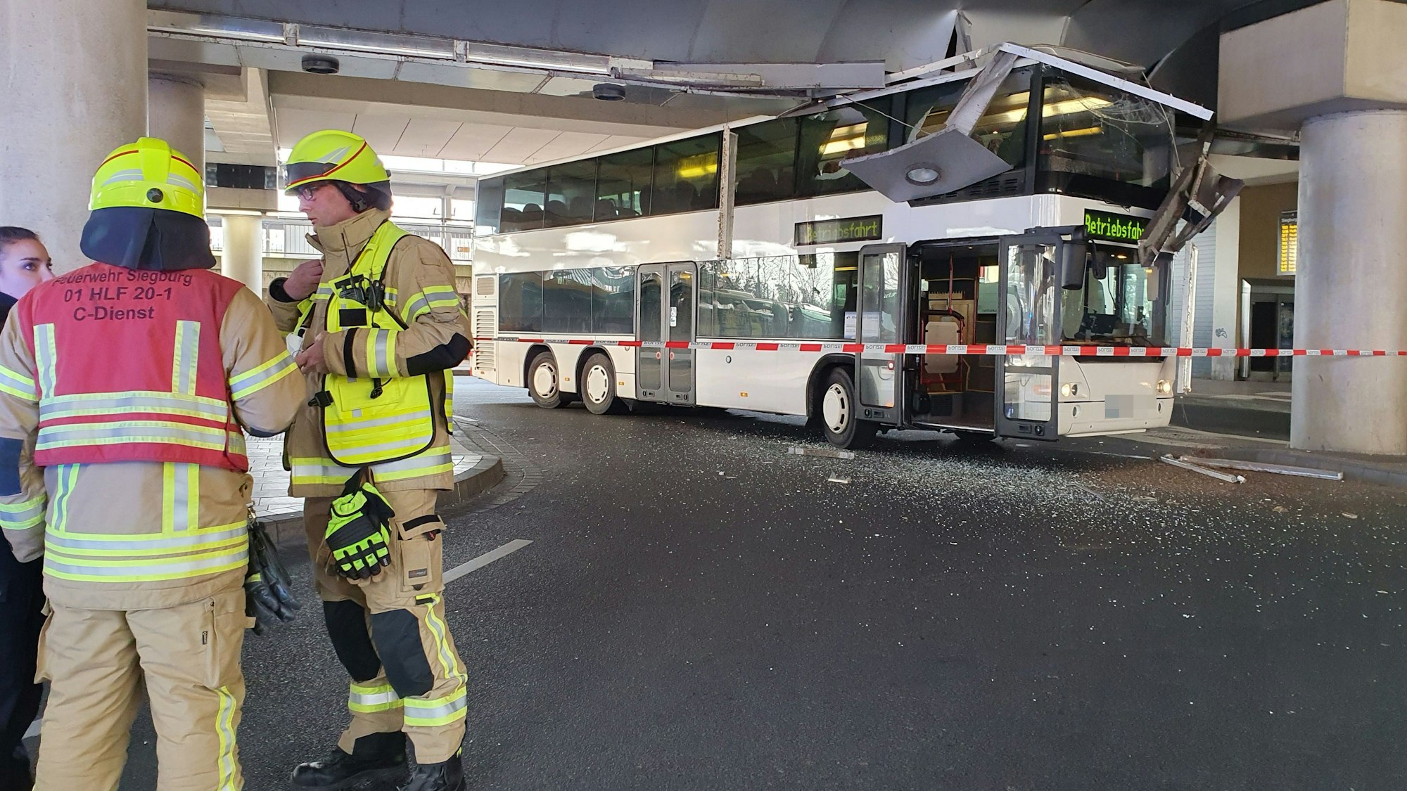 Feuerwehrleute stehen an der Seite, dahinter steht ein Doppeldeckerbus, der sich in einer Unteführung festgefahren hat.