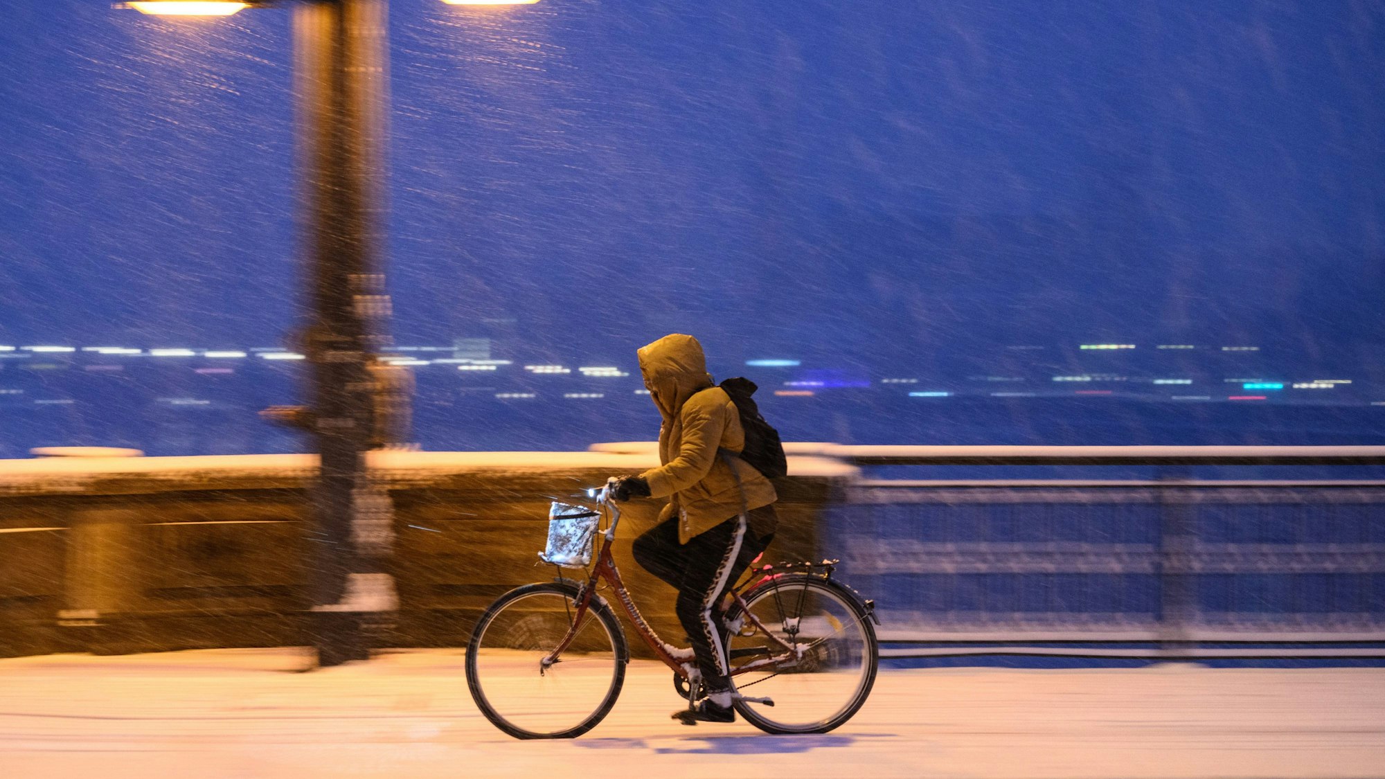 Eine Radfahrerin fährt am Morgen bei Schneefall.