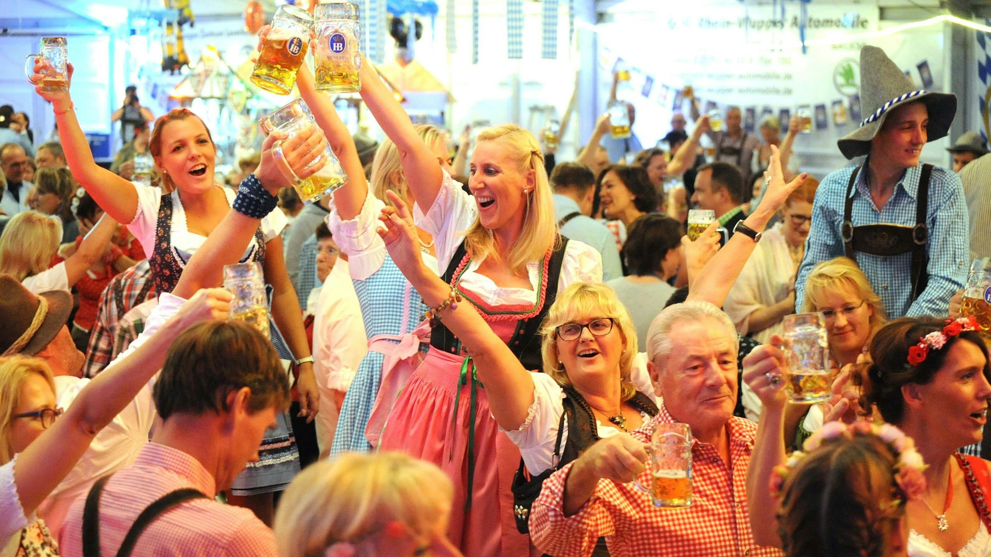 Männer und Frauen in Lederhosen und Dirndl prosten sich im Festzelt mit Bierkrügen zu.