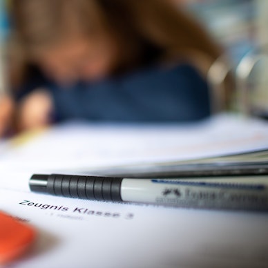 Eine Schülerin der dritten Klasse arbeitet an ihrem Schreibtisch, während ihr Zeugnis auf ihrem Schreibtisch liegt.