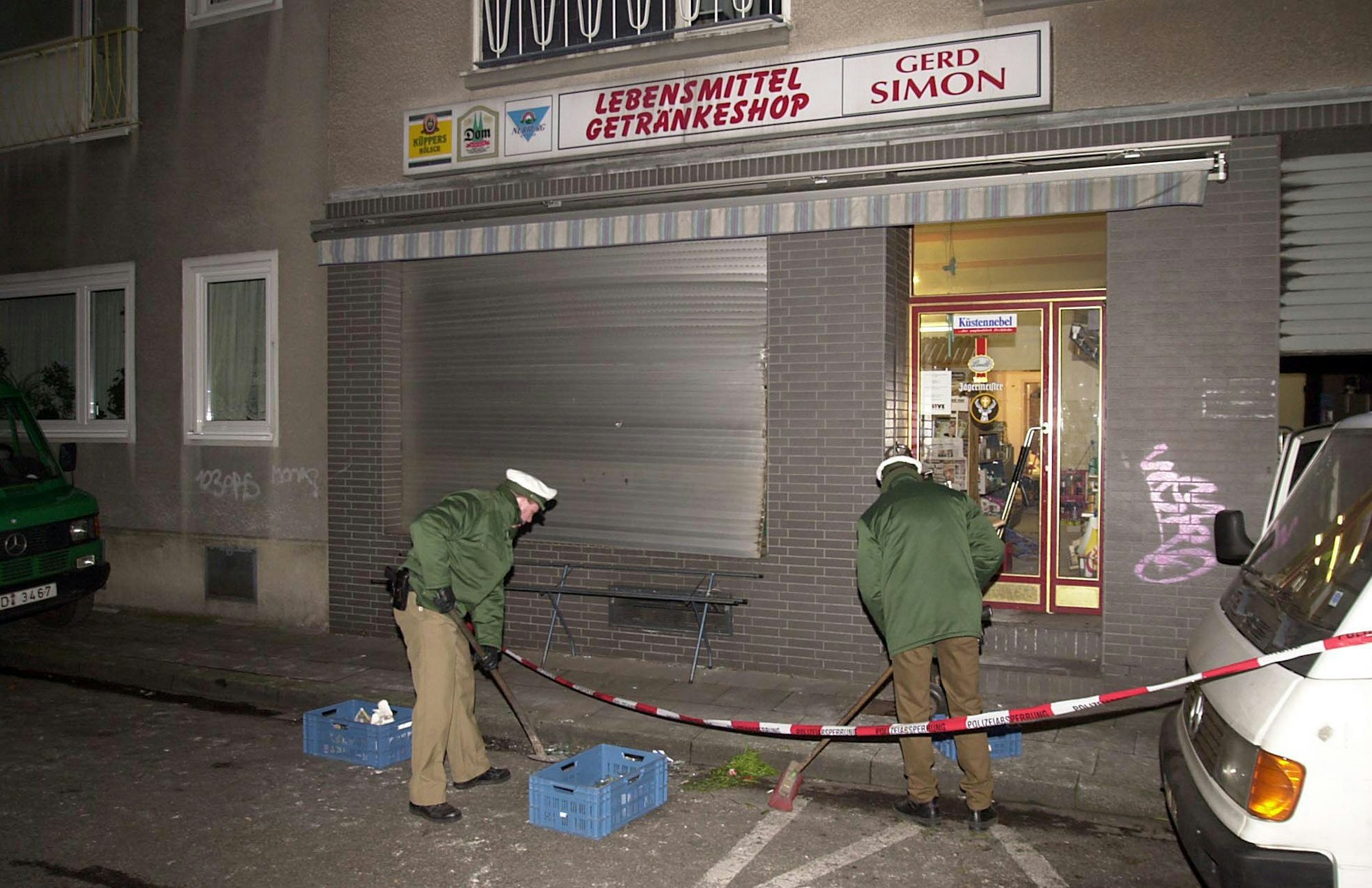 Polizeibeamte kehren nach dem Sprengstoffanschlag auf ein Lebensmittelgeschäft am 19. Januar 2001 in der Probsteigasse in Köln herumliegende Scherben zusammen.