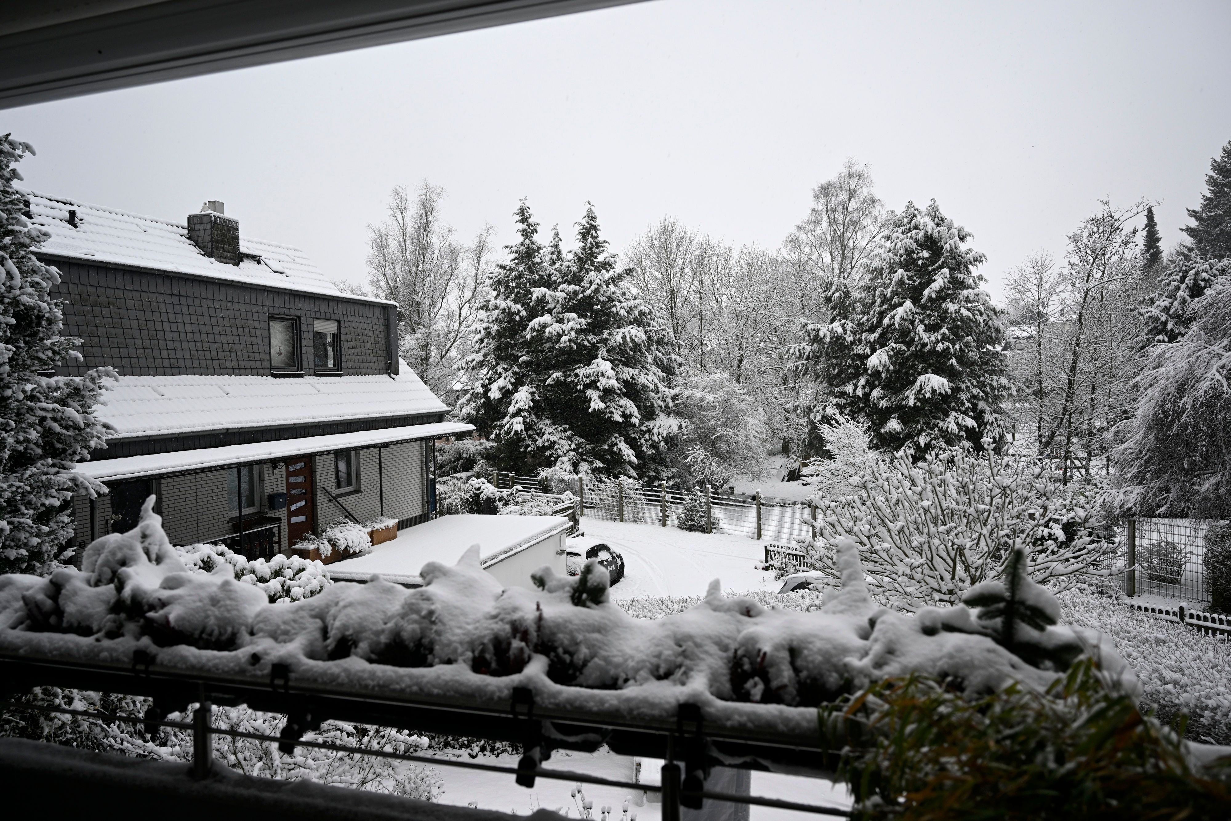 Geländer eines Balkons, Garten und Bäume sind mit Schnee bedeckt.