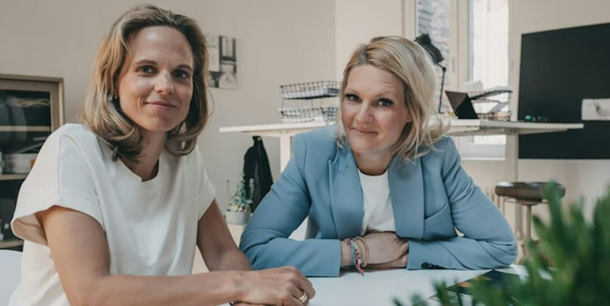 Die beiden Gründerinnen von Badesofa Natalie Steger (links) und Annika Götz sitzen an einem Besprechungstisch.