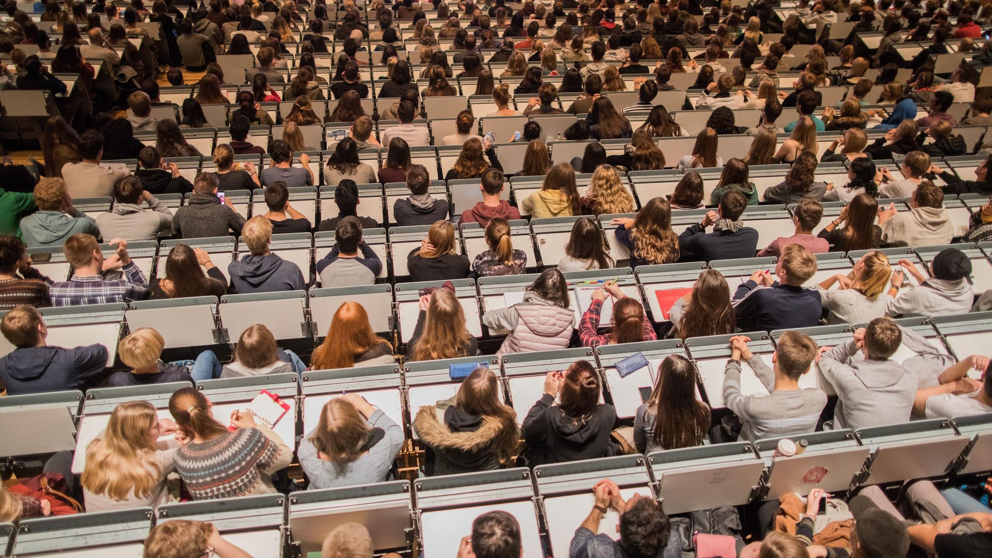 Studenten verfolgen im Hörsaal im Hauptgebäude der Universität zu Köln die Erstsemesterbegrüßung.