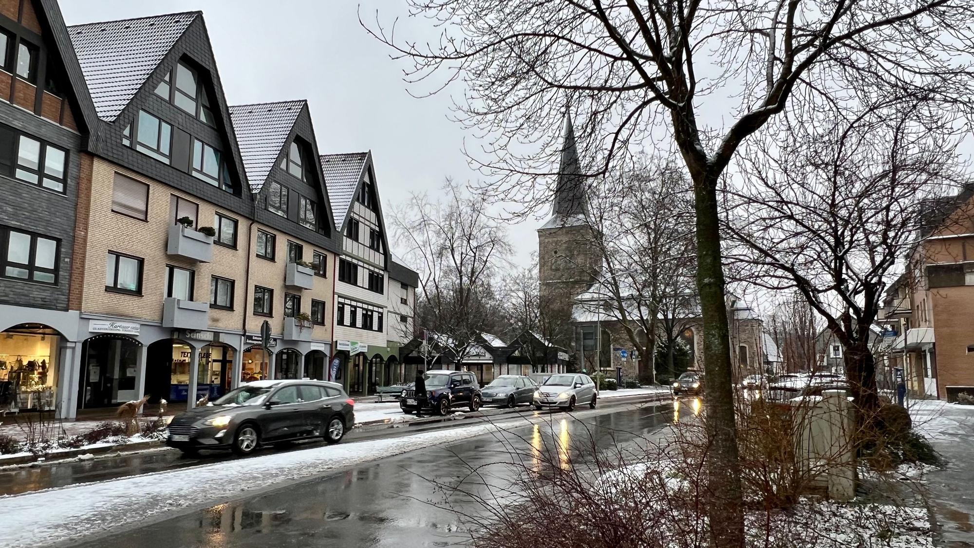 Eine Straße, am Rand liegt Schnee, auf Gehwegen und Häusern auch. Die Straße ist geräumt.