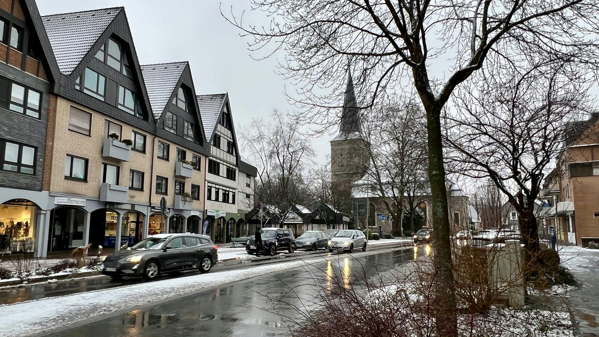 Eine Straße, am Rand liegt Schnee, auf Gehwegen und Häusern auch. Die Straße ist geräumt.