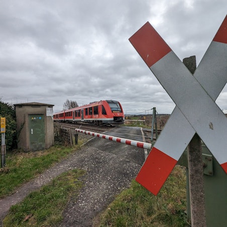 EIn Zug fährt an einem beschrankten Bahnübergang mit Andreaskreuz über das Gleis.