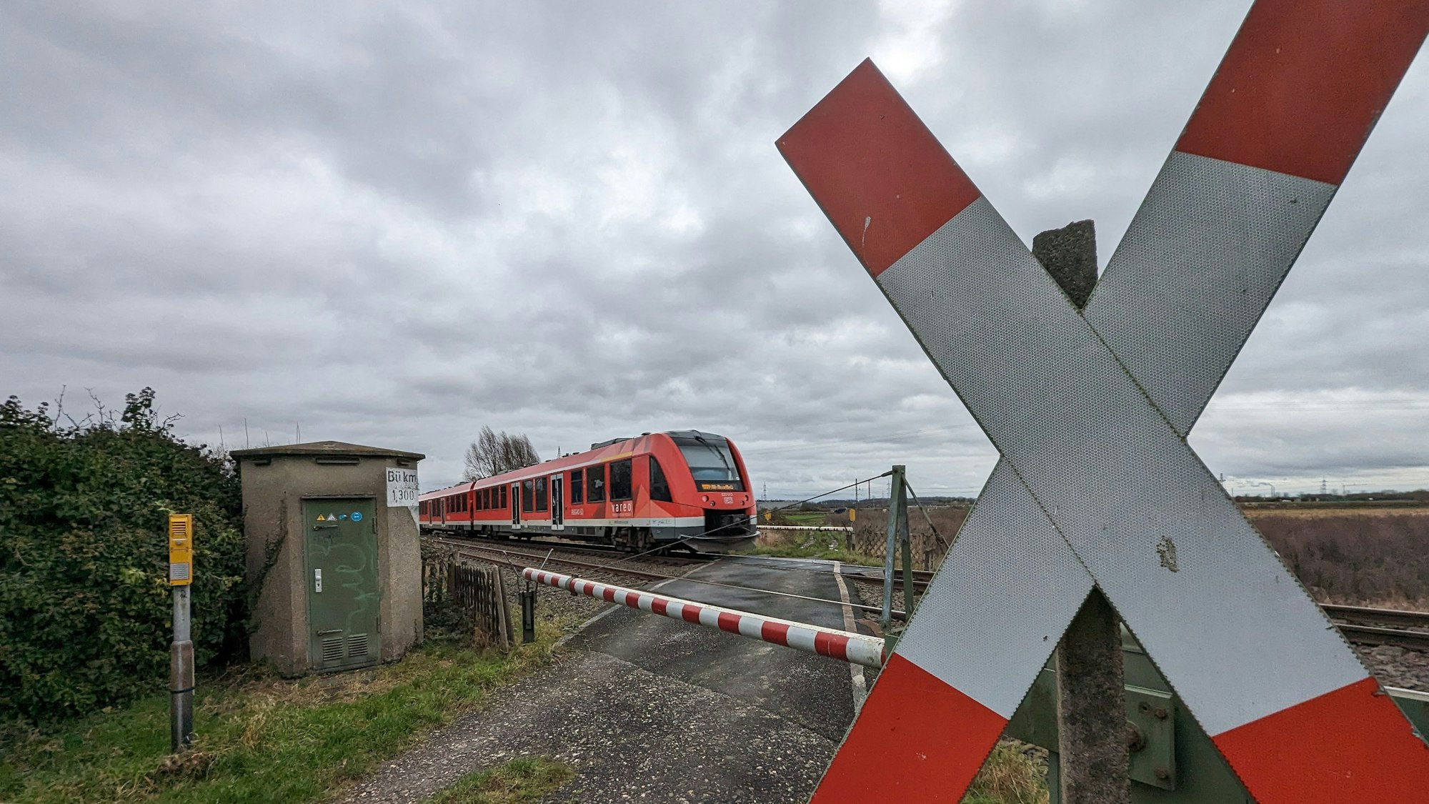 EIn Zug fährt an einem beschrankten Bahnübergang mit Andreaskreuz über das Gleis.