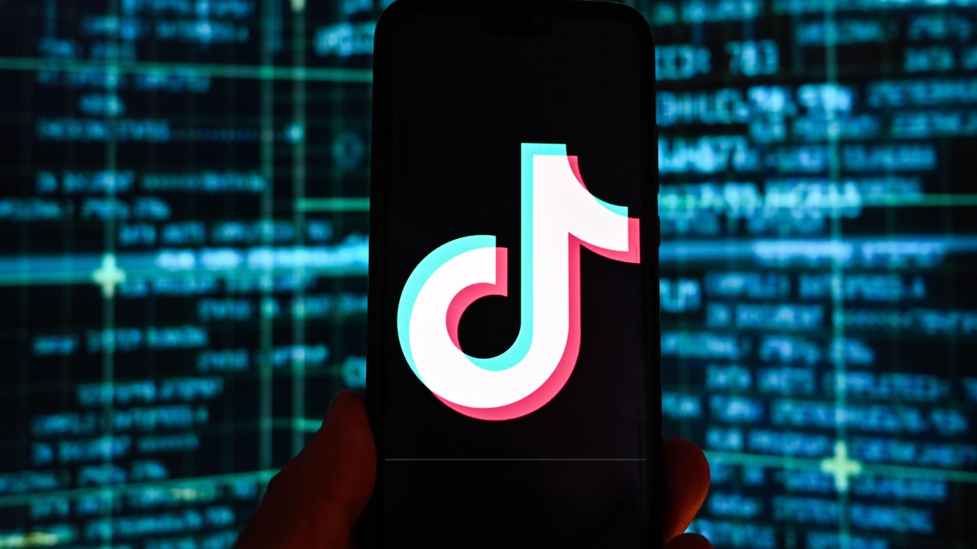 Das Logo der Video-App TikTok ist auf einem Smartphone vor einem Bildschirm mit Börsenkursen im Hintergrund zu sehen.