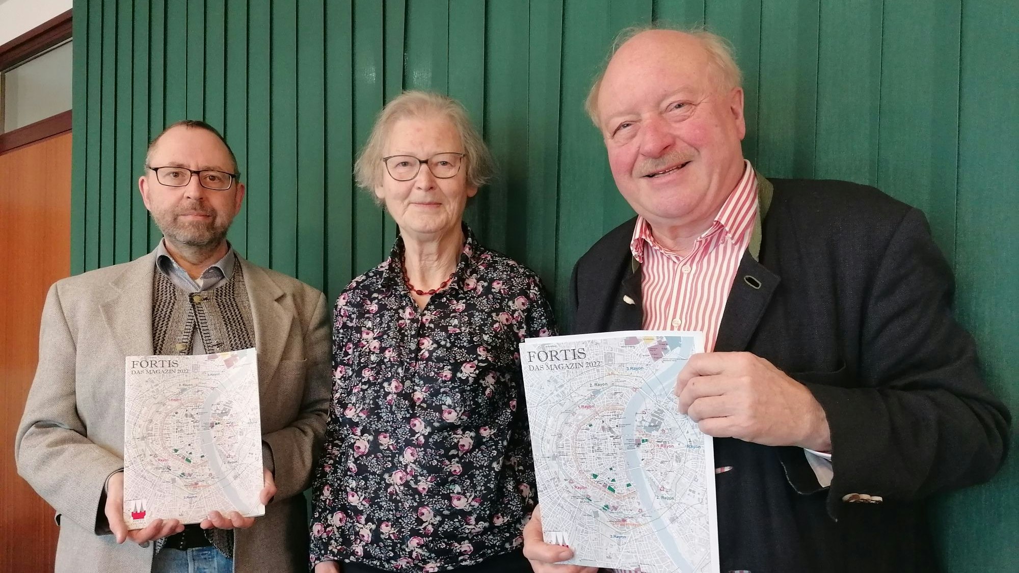 Alexander Hess, Henriette Meynen und Konrad Adenauer mit dem Magazin in der Hand vor einer grünen Wand.