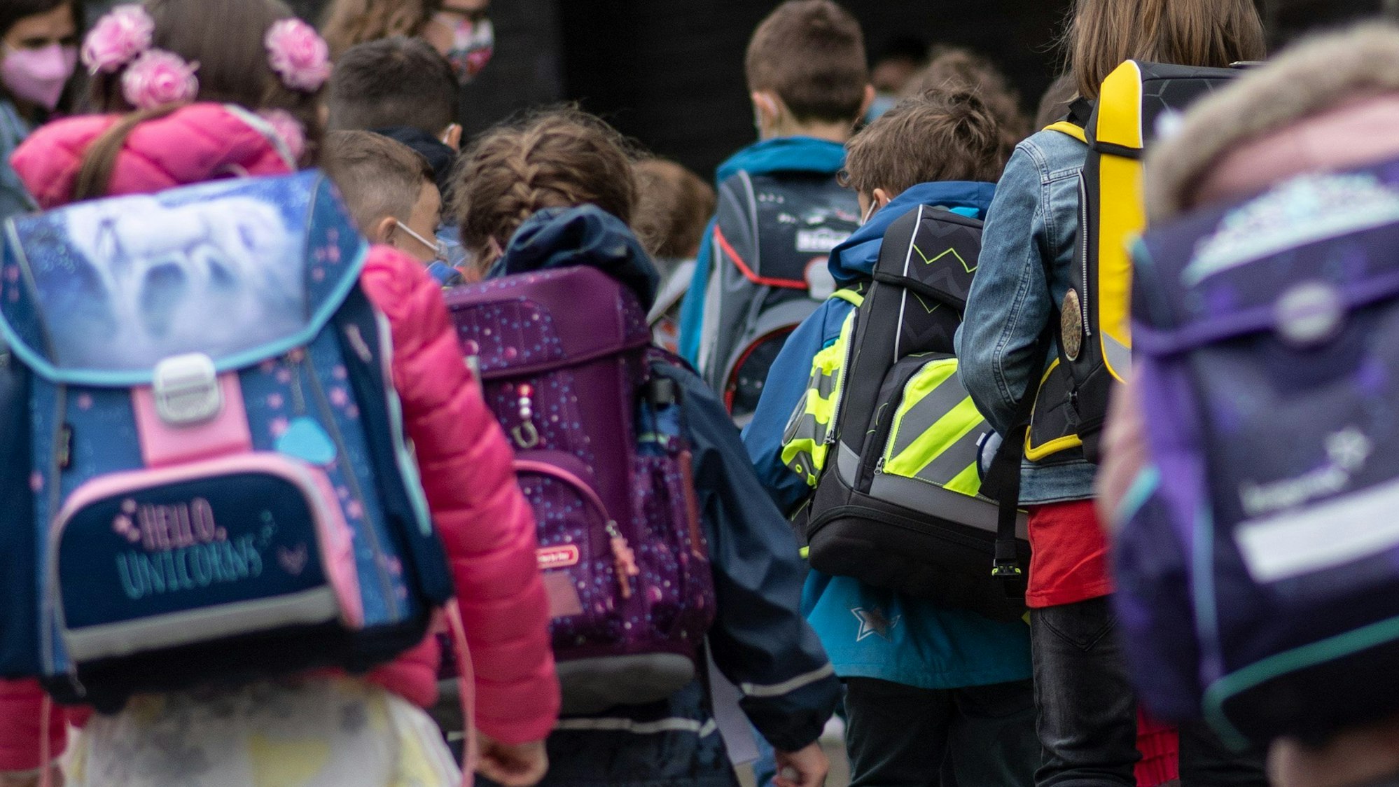 Eine Gruppe von Erstklässler sind mit ihren Schulrucksäcken von hinten zu sehen.