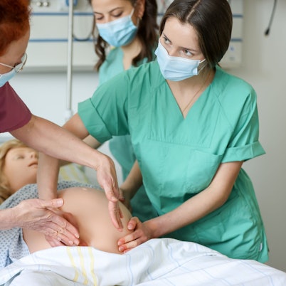 Zwei Studentinnen üben das Ertasten der Lage eines Kindes an einer schwangeren Übungspuppe.