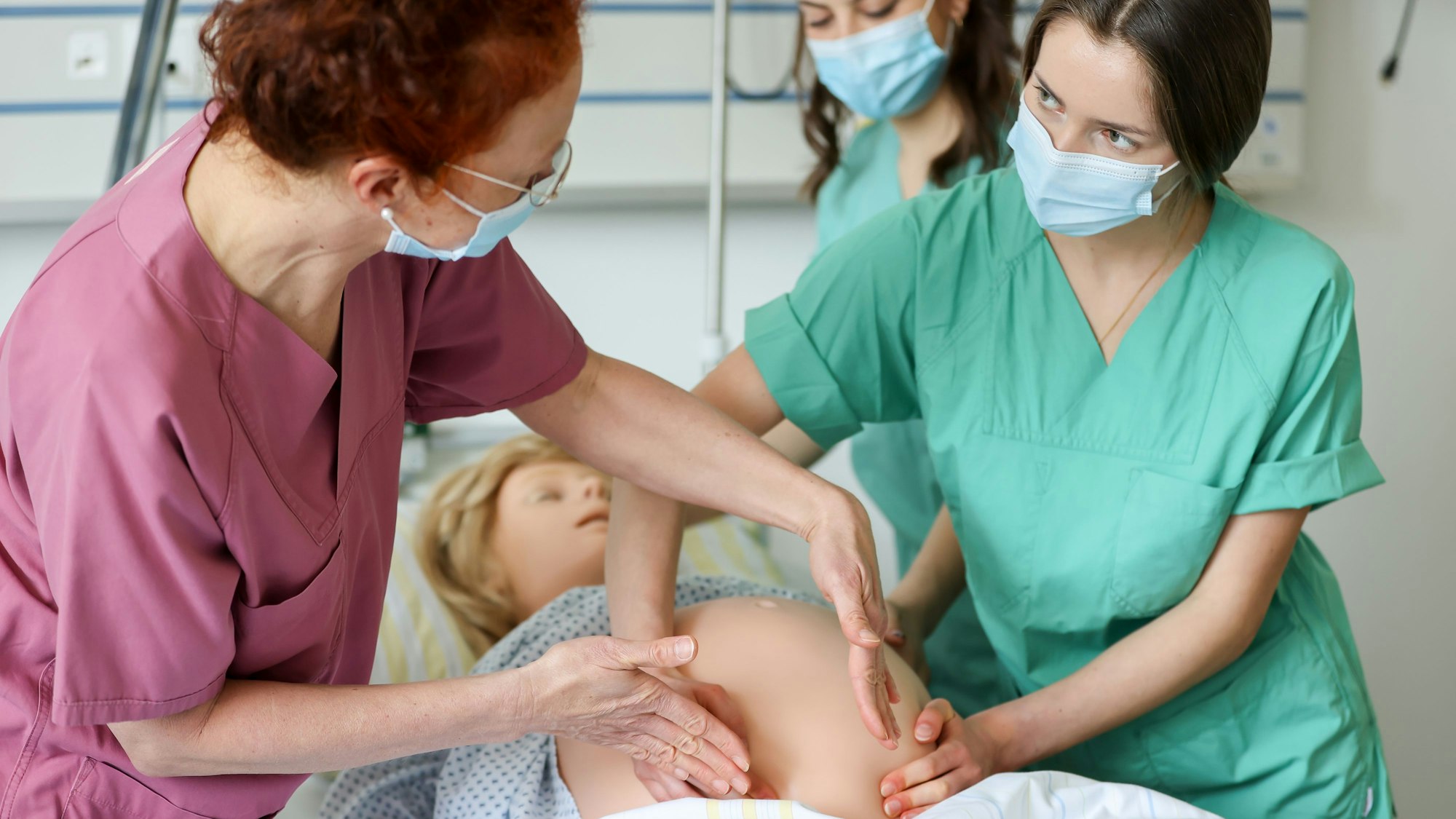 Zwei Studentinnen üben das Ertasten der Lage eines Kindes an einer schwangeren Übungspuppe.