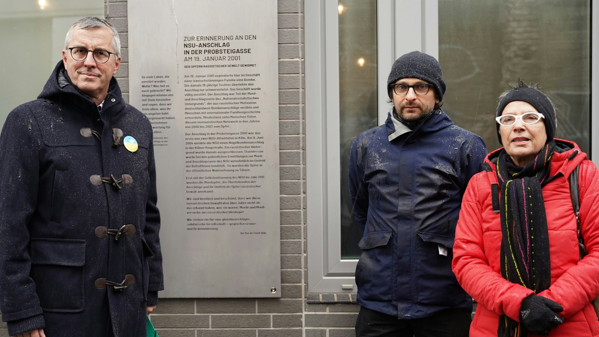 Andreas Wolter, Daniel Poštrak und Edith Lunnebach stehen vor der Gedenktafel zur Erinnerung an den NSU-Sprengstoffanschlag vom 19. Januar 2001 in Köln-Mülheim.