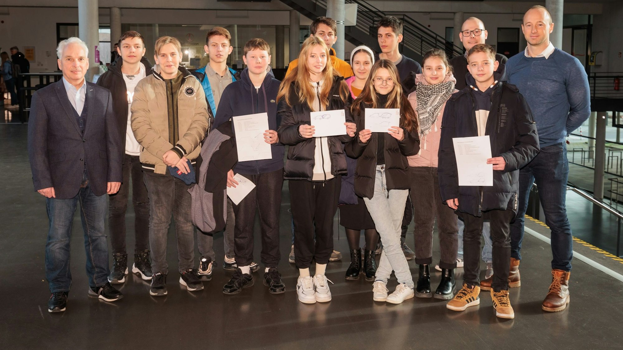 Schülerinnen, Schüler und Lehrer stehen zusammen, einige halten ein Diplom vor sich.