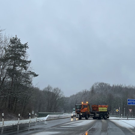 Das Foto zeigt ein orange-farbiges Streufahrzeug, das den Bereich einer Autobahnauffahrt streut und räumt.
