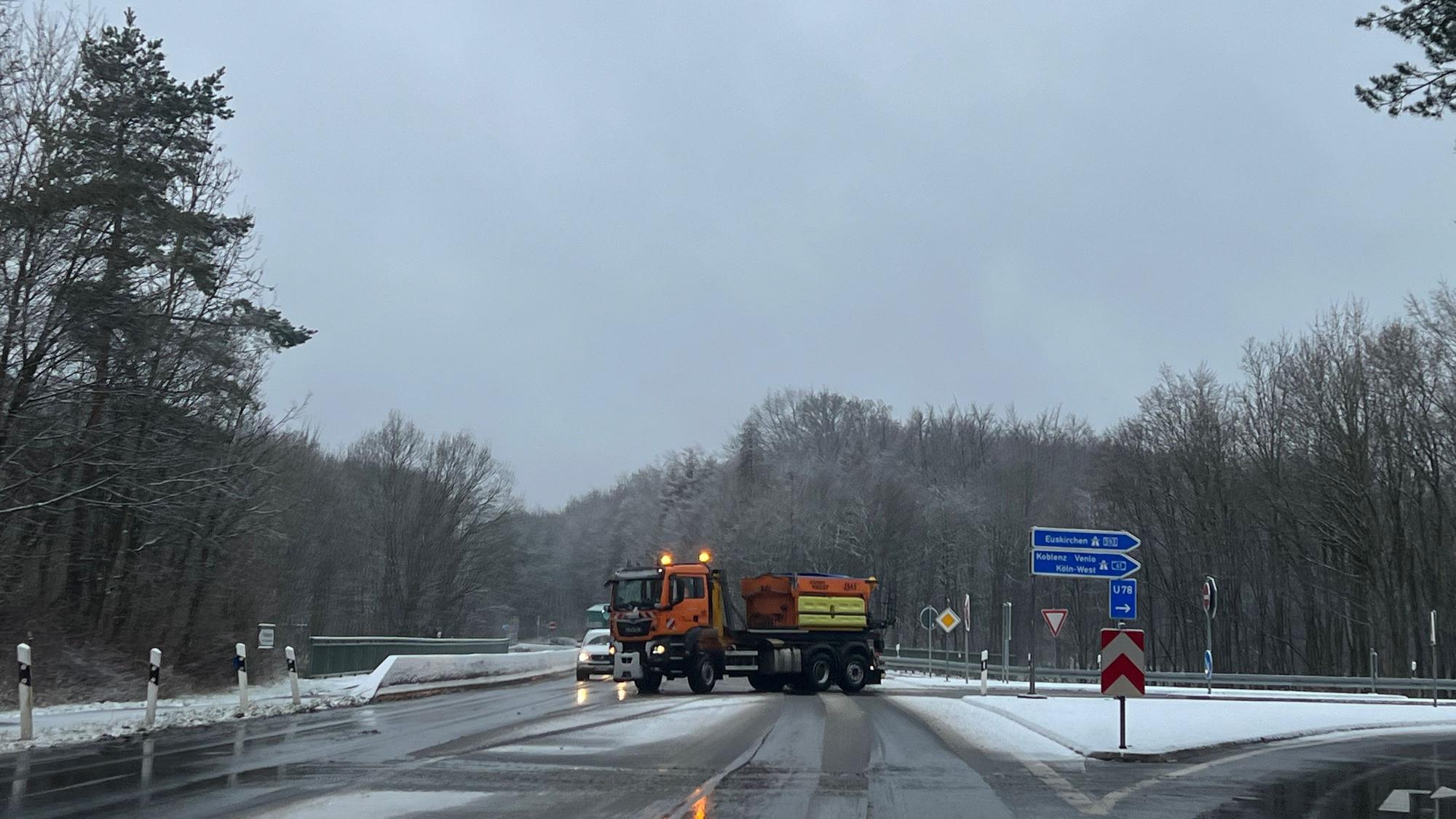 Das Foto zeigt ein orange-farbiges Streufahrzeug, das den Bereich einer Autobahnauffahrt streut und räumt.