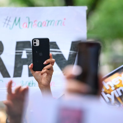 Ein Smartphone wird vor einem Plakat in die Höhe gehalten auf einer Solidaritätskundgebung nach dem Tod von Iranerin Mahsa Amini.