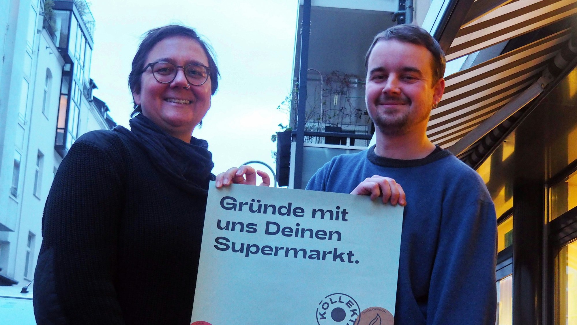 Miriam Schifferman und Malte Garrecht halten ein Werbeplakat in der Hand.