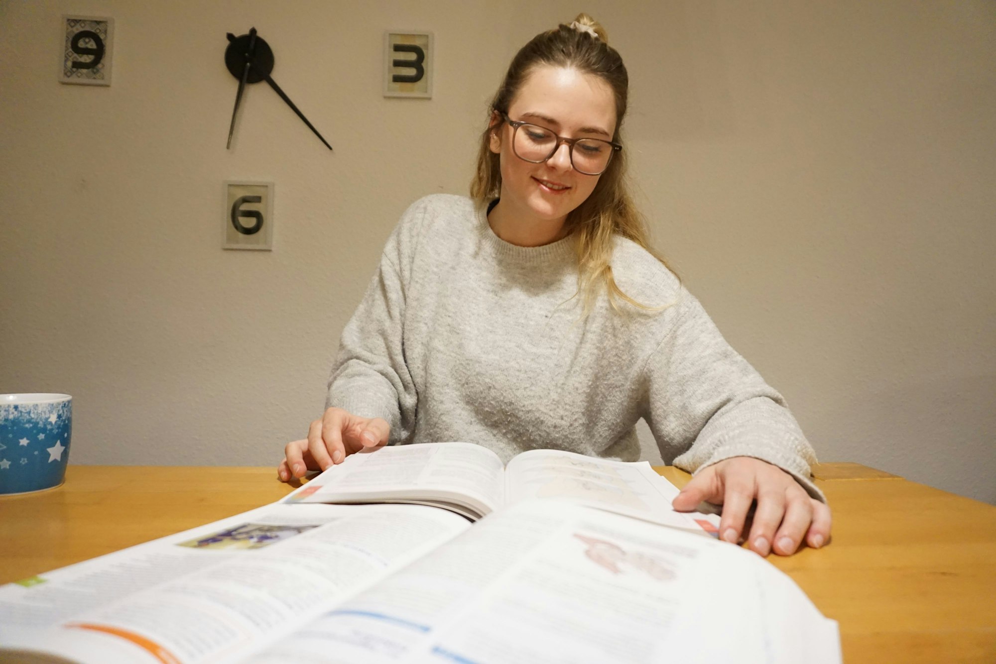 Eine junge Frau sitzt mit ihren Lehrbüchern am Tisch.