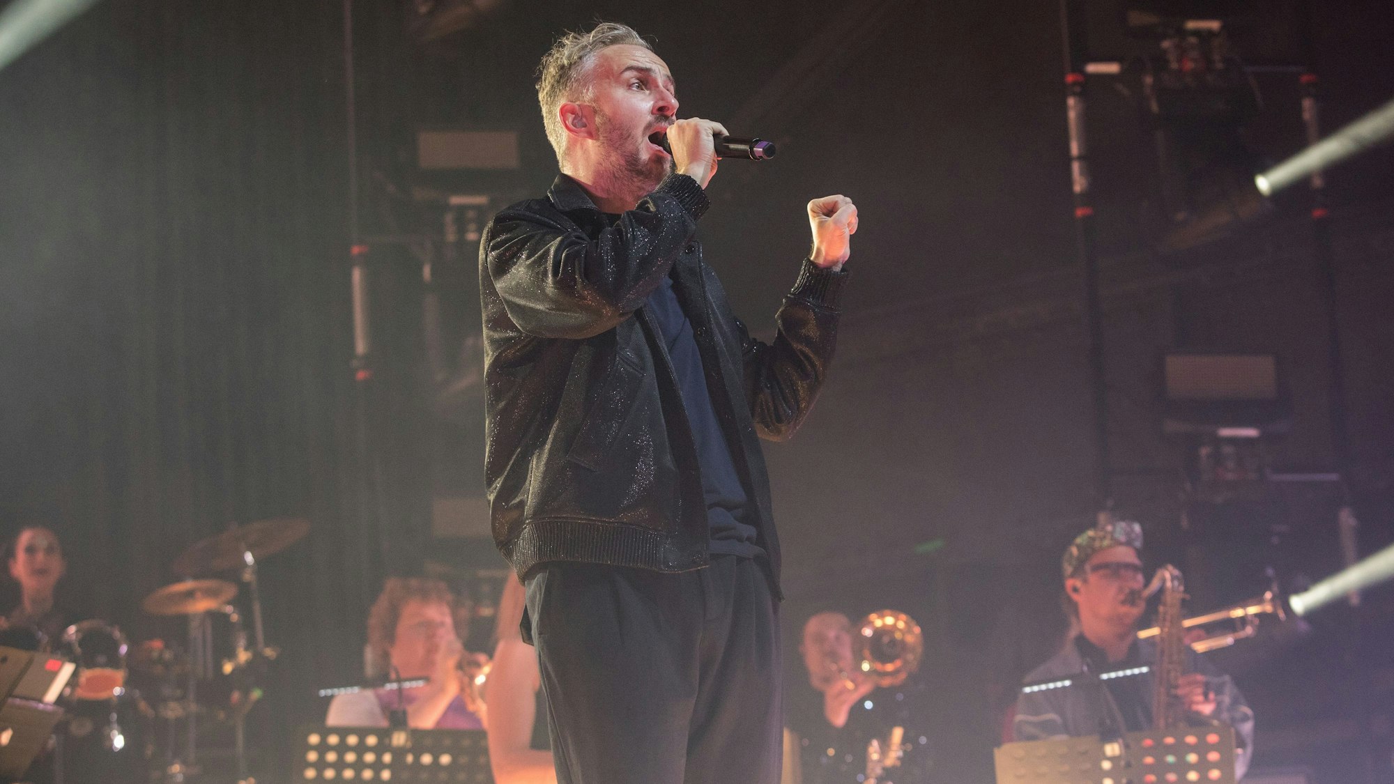 Jan Böhmermann steht singnd vor dem Rundfunktanz-Orchester Ehrenfeld auf der Bühne des Palladium in Köln-Mülheim.