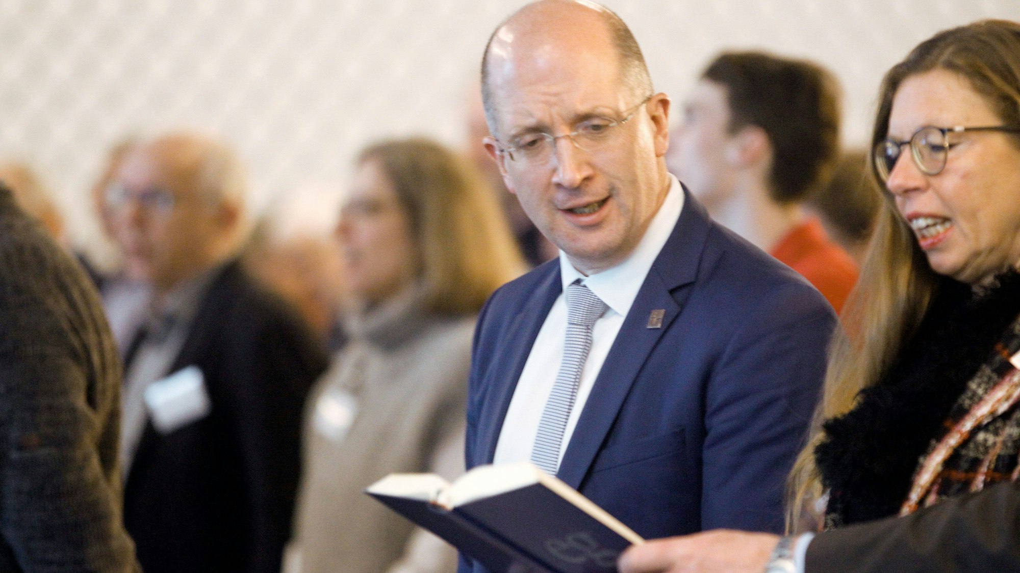 Thomas Latzel steht singend neben einer Frau, die ein Gesangsbuch in die Mitte hält, aus dem er abliest.